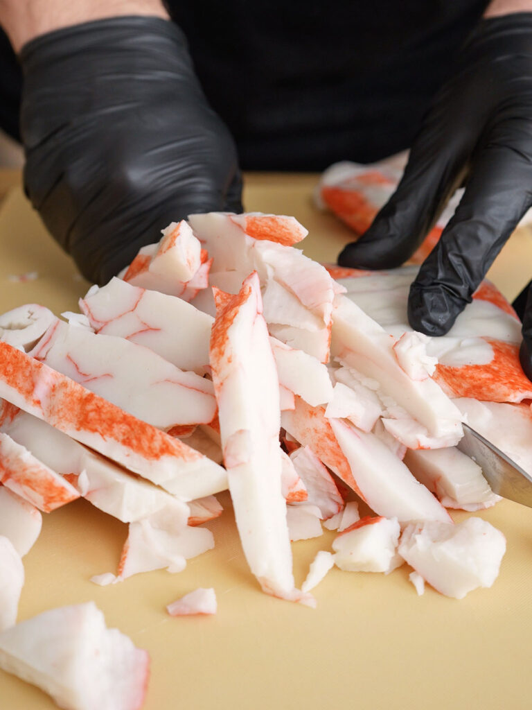 Close up of shredded imitation crab being mixed with whipped cream cheese and green onions in a silver stand mixer bowl to create the creamy crab layer for a California Roll Sushi Bake.