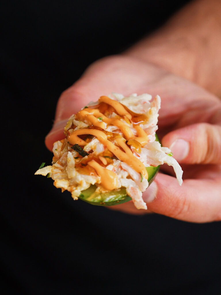 A spoon scooping a portion of California Roll Sushi Bake onto a fresh, crisp slice of cucumber for serving as a low-carb alternative to nori.