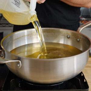 Pouring neutral frying oil from a plastic jug into a large stainless steel pot to prepare for frying homemade Salt and Vinegar Potato Chips.