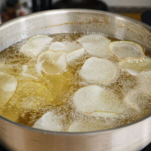 Thinly sliced russet potatoes actively bubbling and frying in 300-degree hot oil to become perfectly crisp homemade Salt and Vinegar Potato Chips.