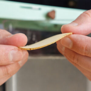 Fingers holding up an ultra-thin, almost translucent slice of raw russet potato cut on a mandoline to ensure the perfect crunch for Salt and Vinegar Potato Chips.