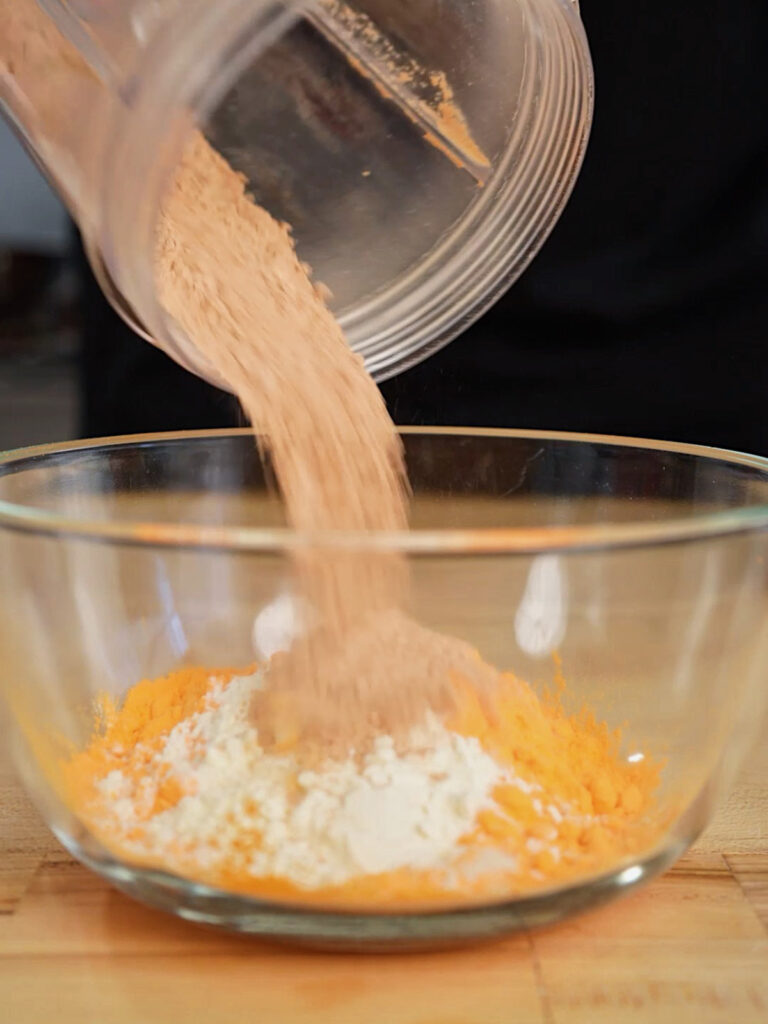 A black gloved hand adds Cheddar Cheese Powder to Roice Bethel's homemade Doritos seasoning, a food science-driven copycat recipe from @noflakeysalt.