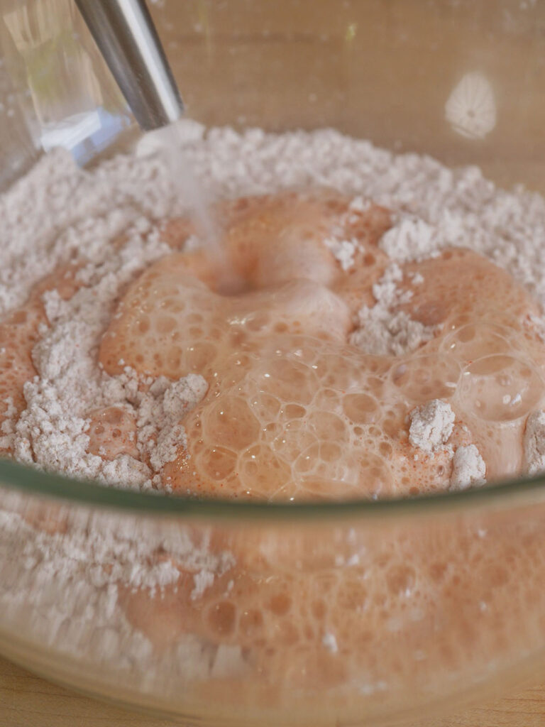 Close-up of highly carbonated sparkling water bubbling as it is poured into a dry flour mixture for homemade McDonald's chicken nugget tempura batter.