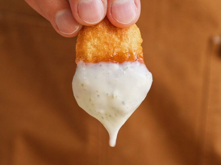 Extreme close-up of a crispy homemade McDonald's chicken nugget dripping with thick, creamy Wingstop copycat ranch dressing.