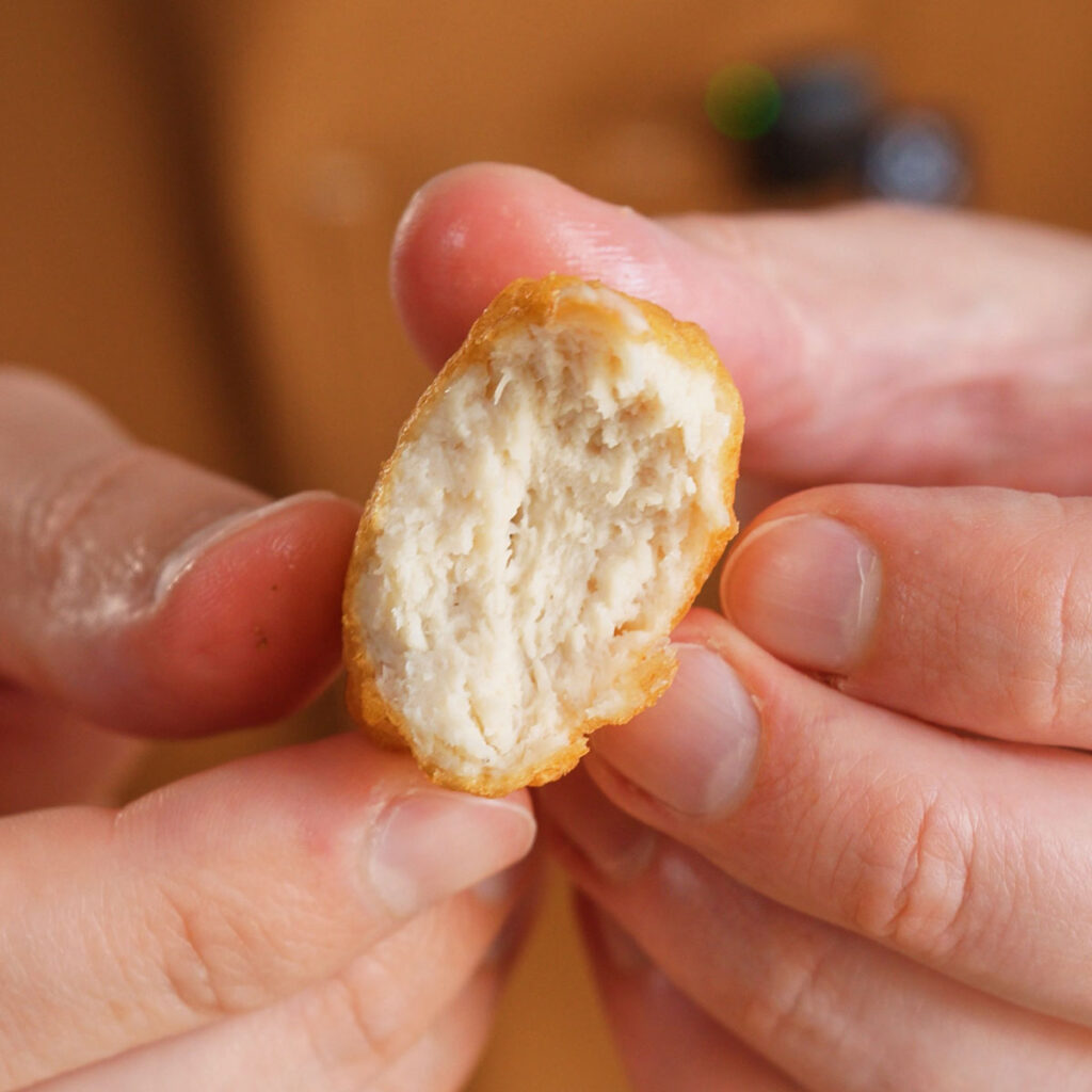 A crispy homemade McDonalds chicken nuggets split in half, revealing a juicy, perfectly bound white meat emulsion interior.