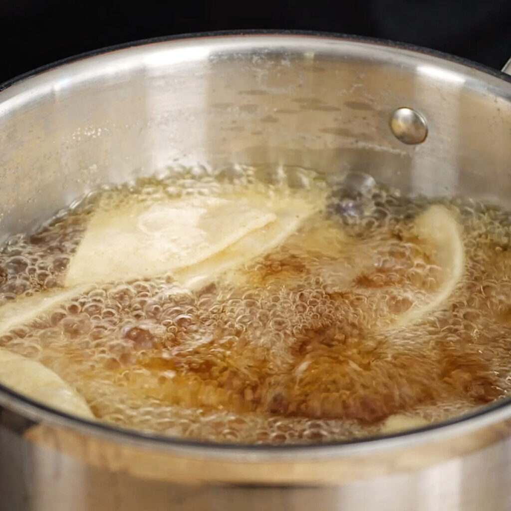 Corn tortilla triangles actively frying and bubbling in hot oil, the first step in Roice Bethel's science-focused homemade Doritos recipe from @noflakeysalt.