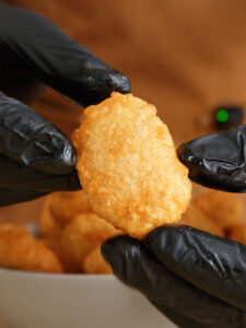 Black-gloved hands presenting a perfectly fried, golden-brown homemade McDonald's chicken nugget.