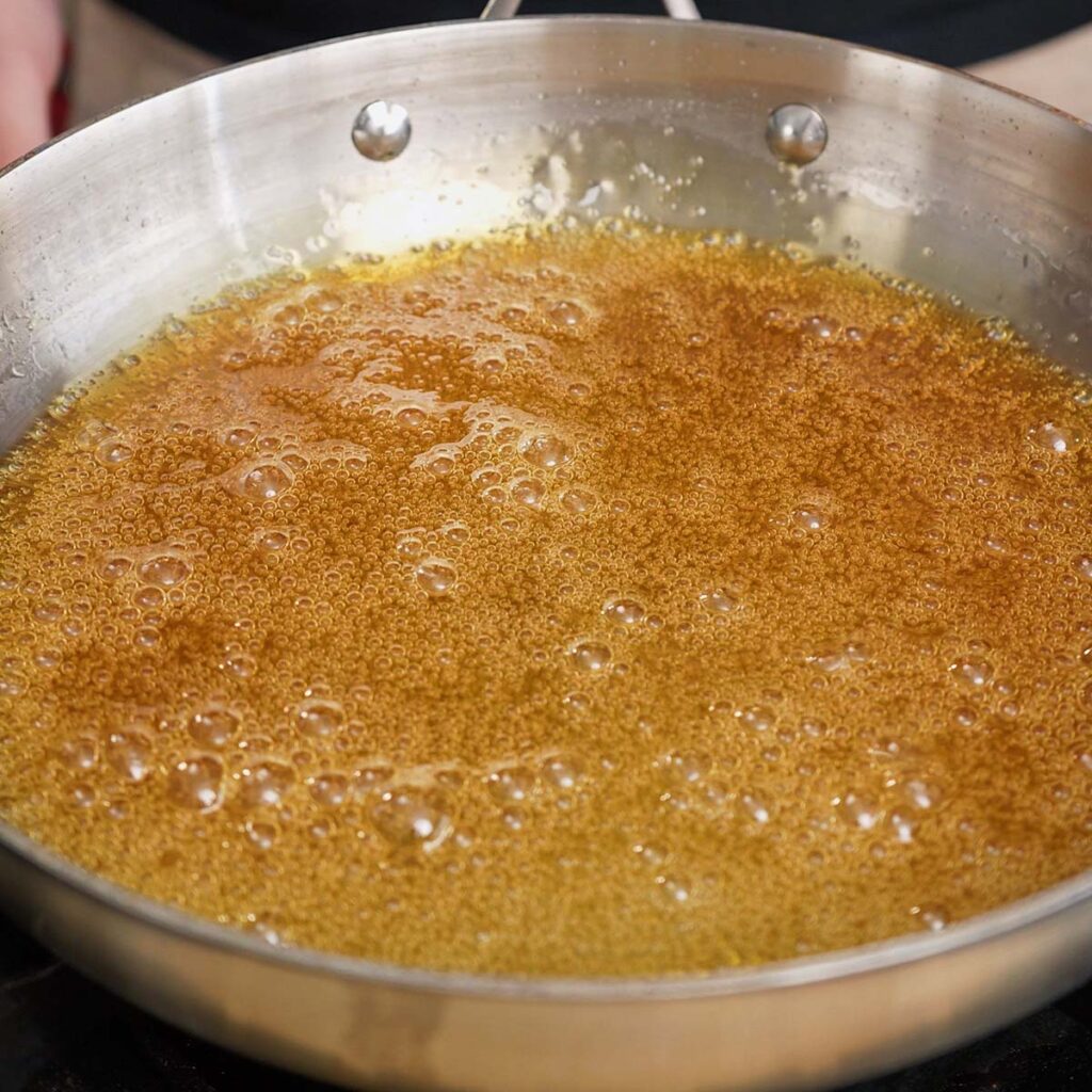 Sugar and water bubbling in a saucepan to create a dark golden caramel for homemade flan.