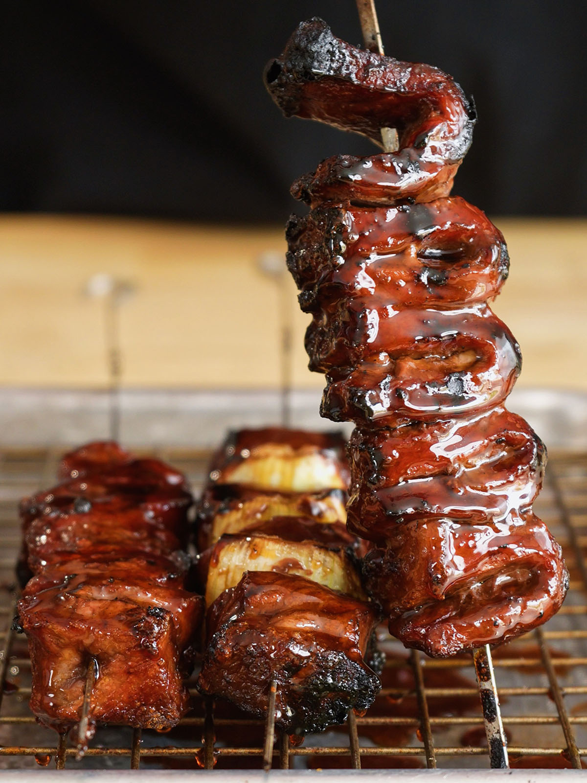 A close-up of a perfectly caramelized, glistening beef and leek skewer held vertically, showcasing the rich, dark tare glaze of a homemade yakitori recipe.