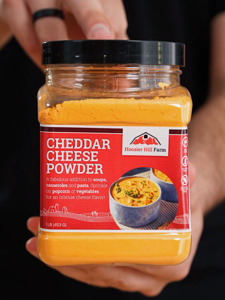 Roice Bethel (@noflakeysalt) holding a jar of Hoosier Hill Farm Cheddar Cheese Powder, the primary base ingredient for his custom Nacho Cheese chip seasoning.