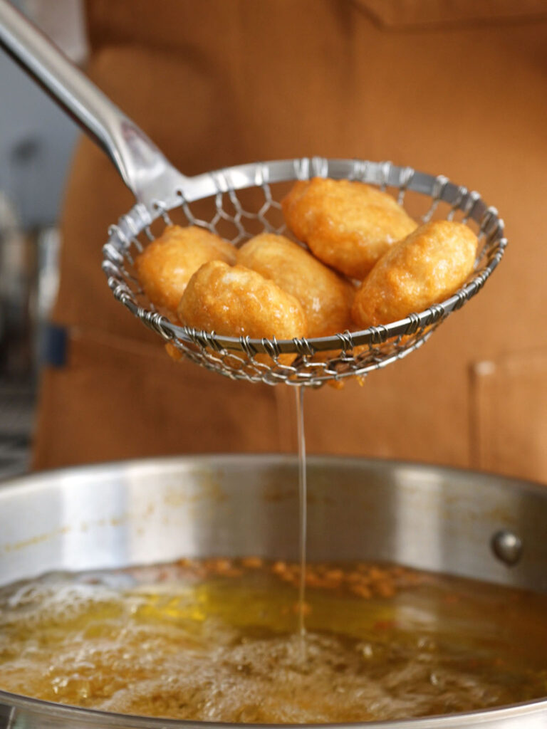 A stainless steel spider skimmer lifting perfectly golden-brown, crispy homemade chicken nuggets out of hot frying oil.