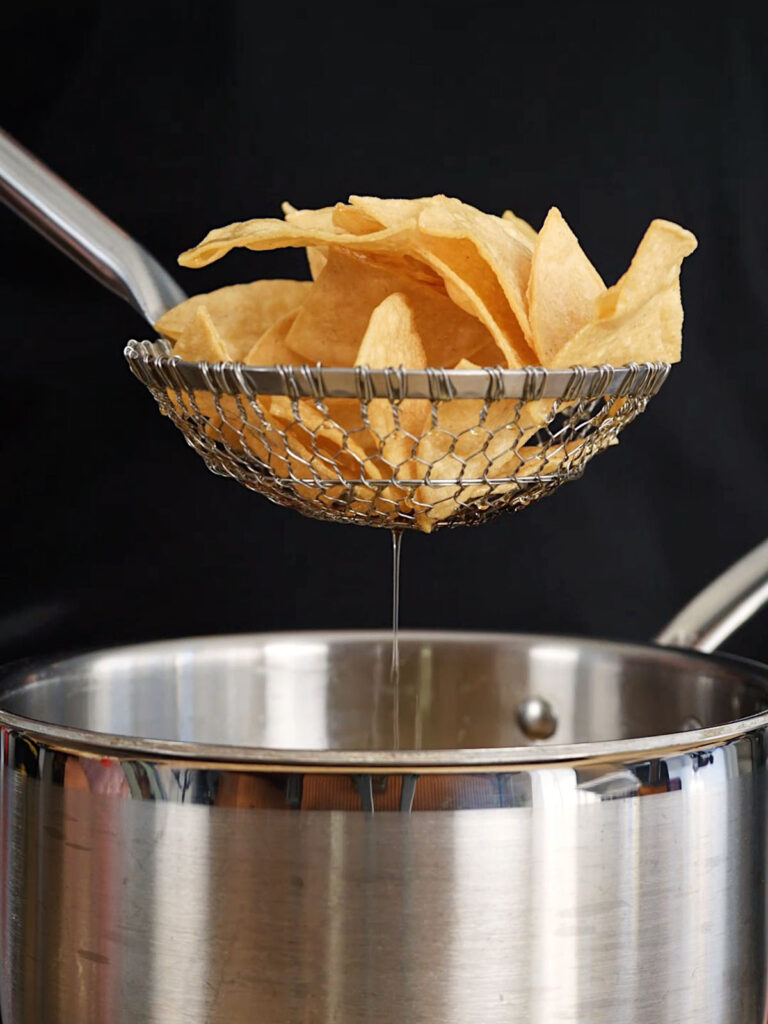 Roice Bethel (@noflakeysalt) using a spider skimmer to lift freshly fried white corn tortilla chips out of 275-degree oil for his from-scratch snack recipe.
