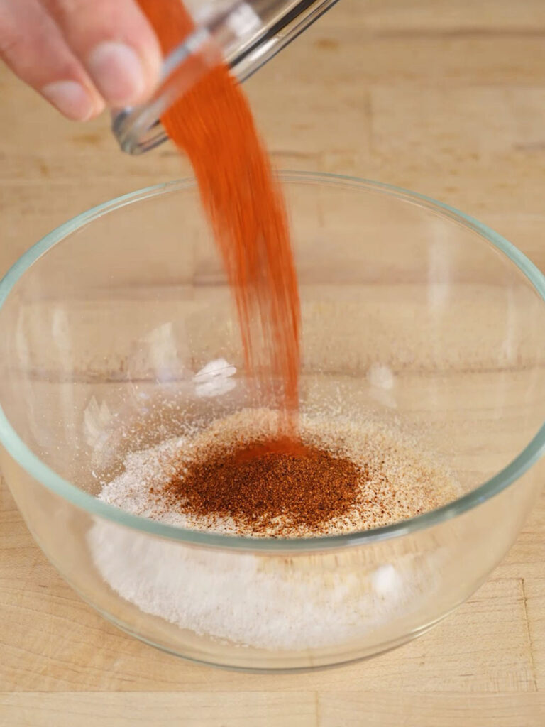 Measuring out spice powders into a small bowl to create a homemade seasoning mix.
