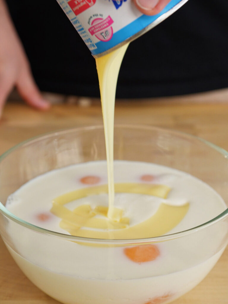 Whisking sweetened condensed milk, eggs, and whole milk in a bowl to create a smooth custard base for homemade flan.