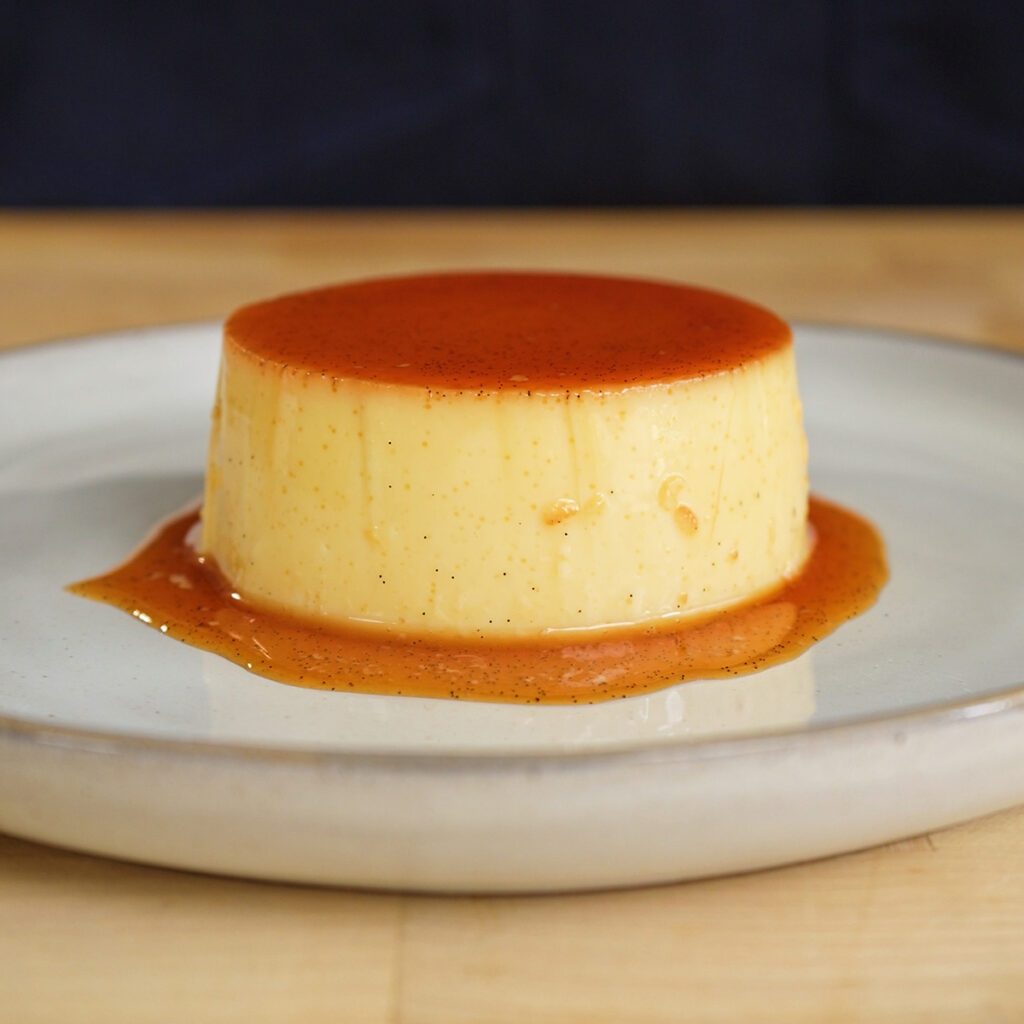 A beautifully unmolded homemade flan on a plate, featuring a glossy dark caramel sauce pooling around the edges.