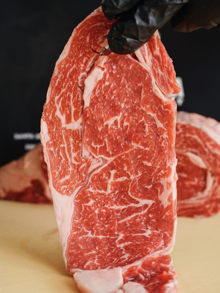 A highly marbled raw beef steak from La Carniceria Meat Market, ready to be sliced for a homemade yakitori recipe.
