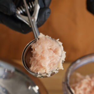 A metal cookie scoop holding perfectly blended ground chicken paste, ready to be shaped into nuggets.