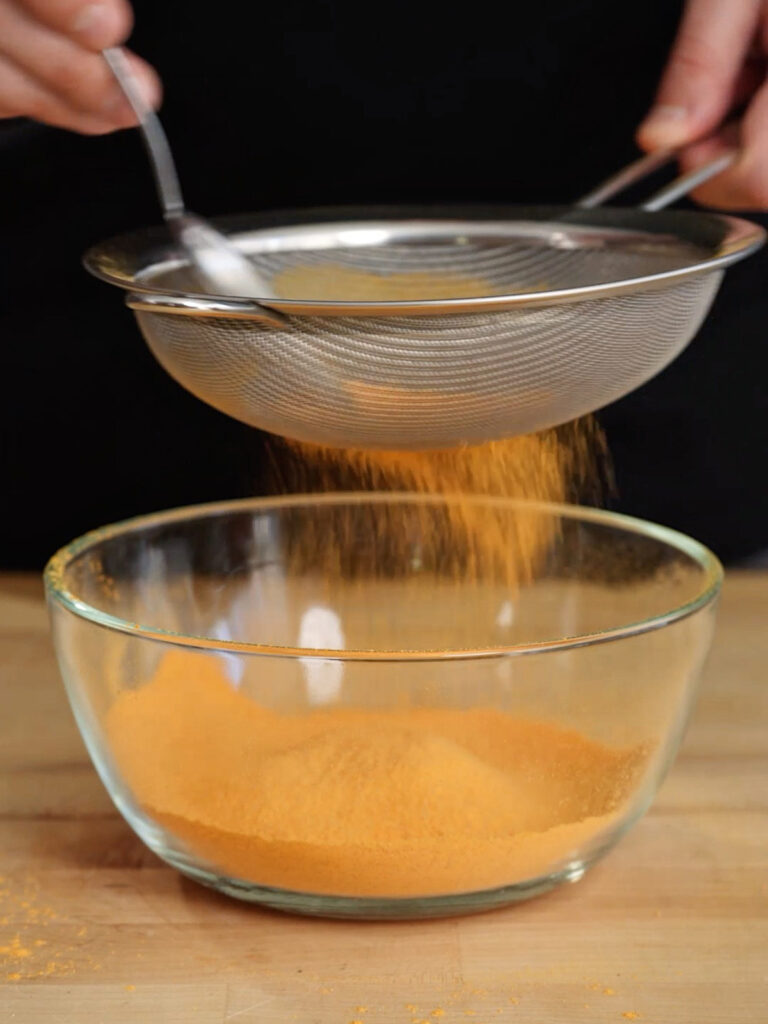 Sifting a blend of MSG, spices, and cheese powders through a fine-mesh strainer to ensure a smooth coating for @noflakeysalt's Nacho Cheese copycat chips.