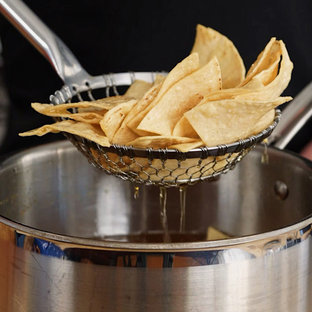 A spider skimmer lifting freshly fried corn tortilla chips from hot oil.