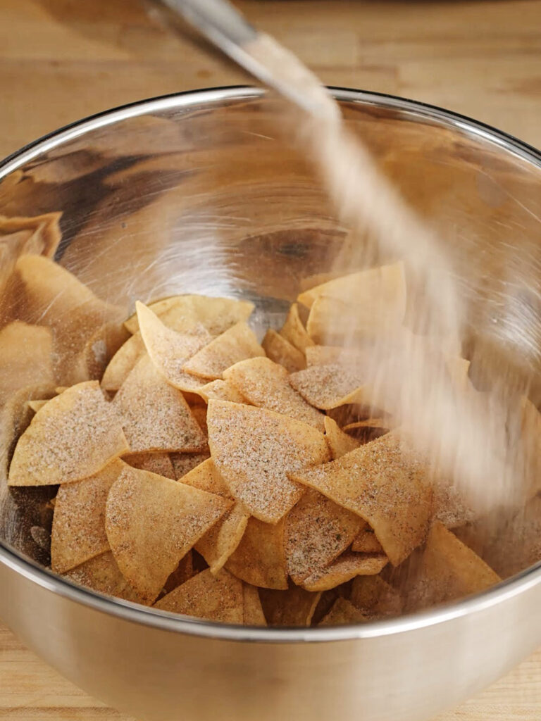 Sprinkling the Cool Ranch spice blend over a bowl of freshly fried chips.