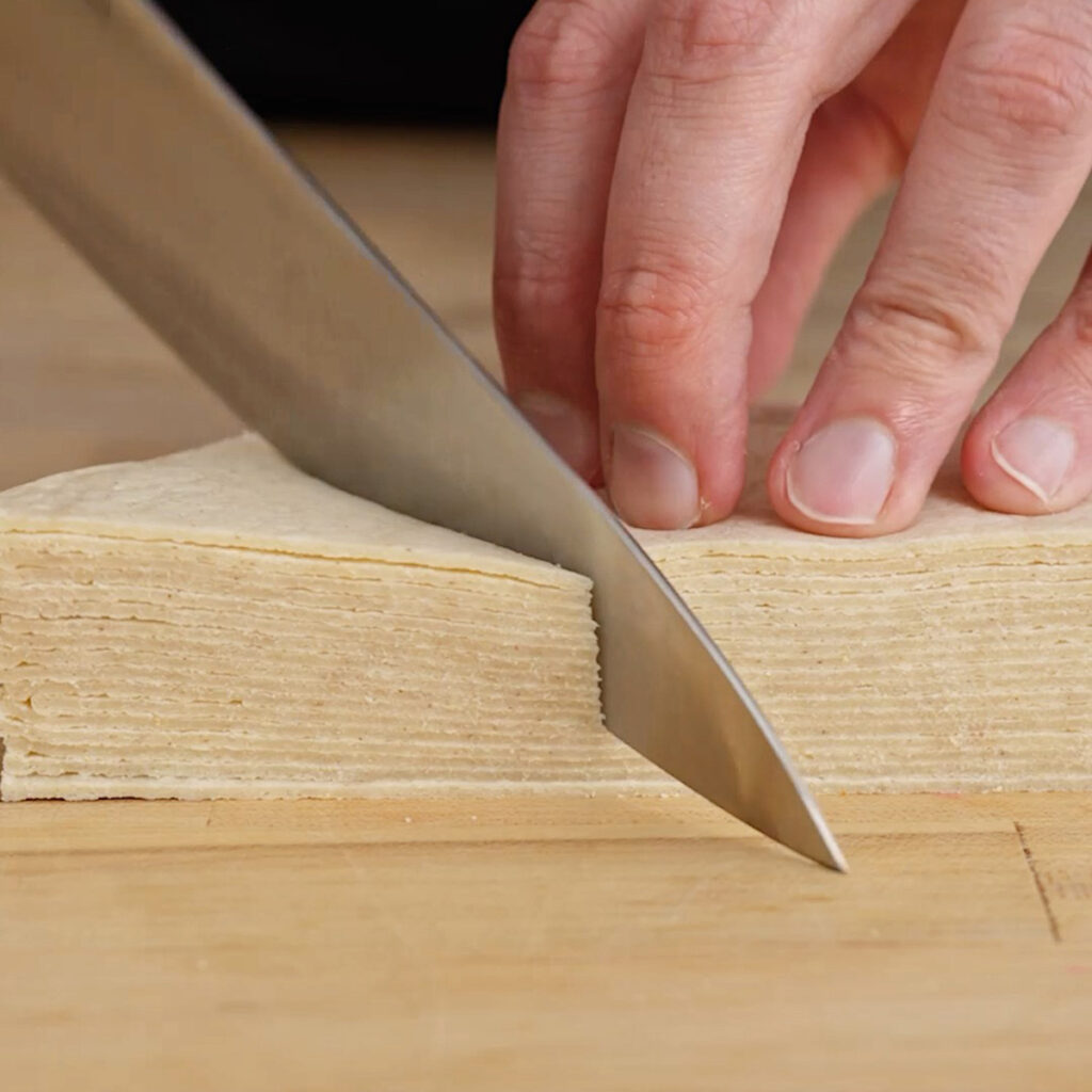 A person stacking cut white corn tortilla triangles in preparation for frying.