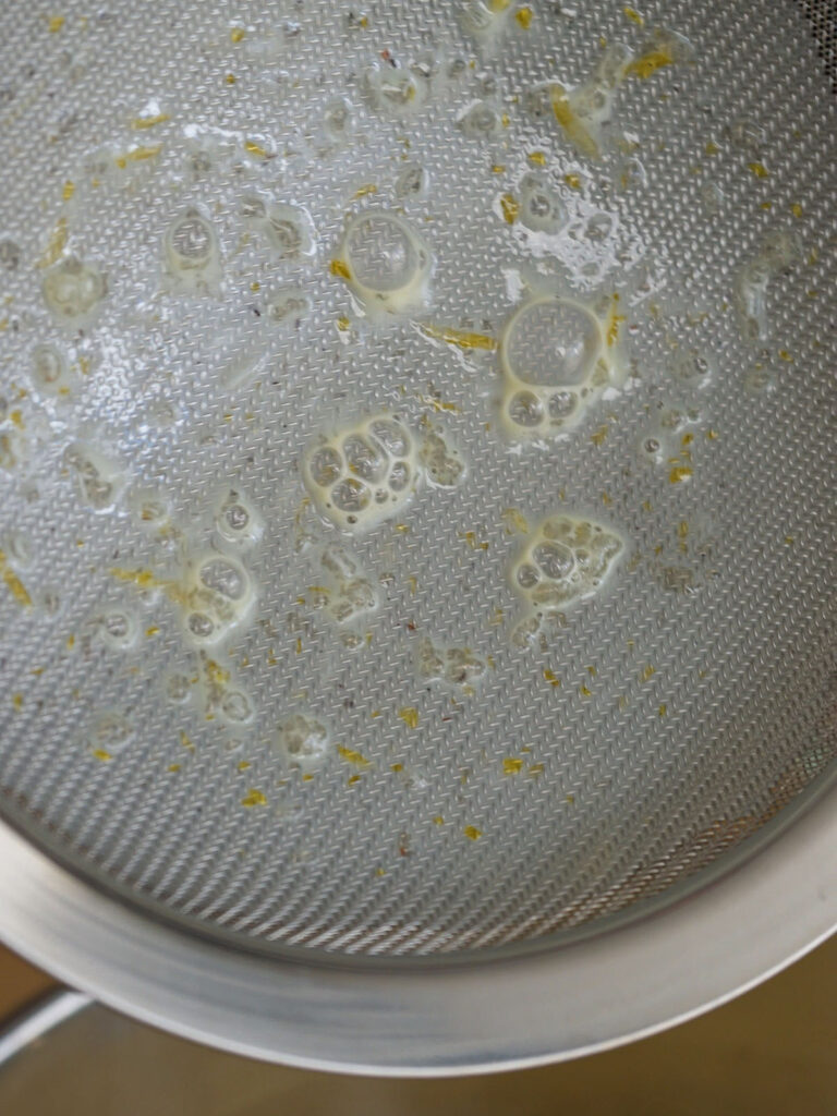 A fine mesh strainer catching egg solids to ensure an ultra-smooth, restaurant-quality texture for homemade flan.