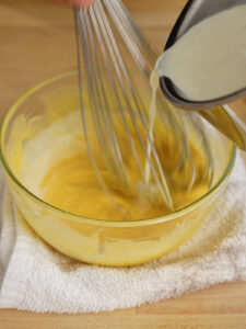 Slowly pouring hot heavy cream into an egg yolk mixture to temper the homemade creme brulee custard.