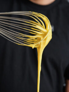 A wire whisk lifting pale, creamy egg yolks and sugar for a homemade creme brulee base.