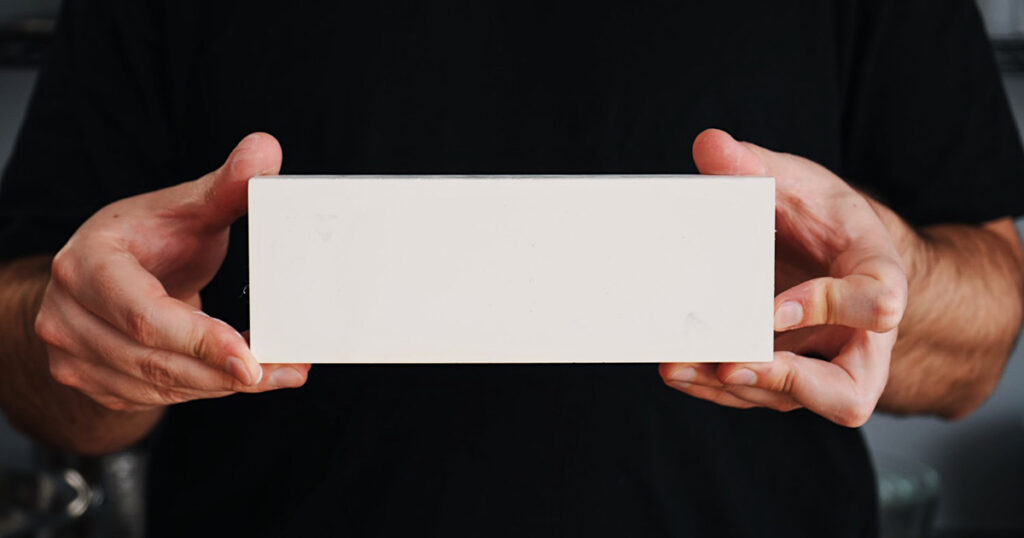 Hands holding a white 1000-grit whetstone for kitchen knife sharpening