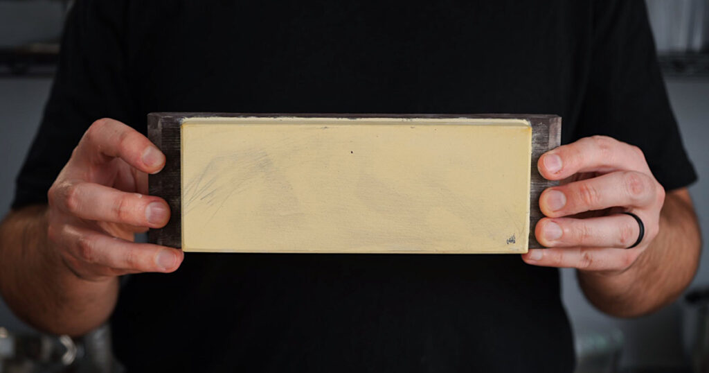 Hands holding an 8000-grit yellow whetstone for high-end knife sharpening