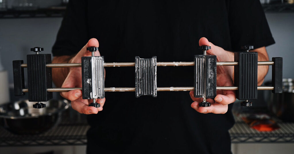 Hands holding an adjustable whetstone sink bridge for sharpening equipment