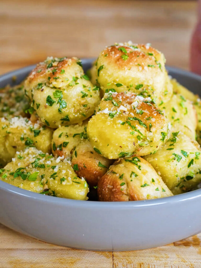 A close-up view of freshly baked garlic knots topped with minced garlic, parsley, and grated parmesan cheese.