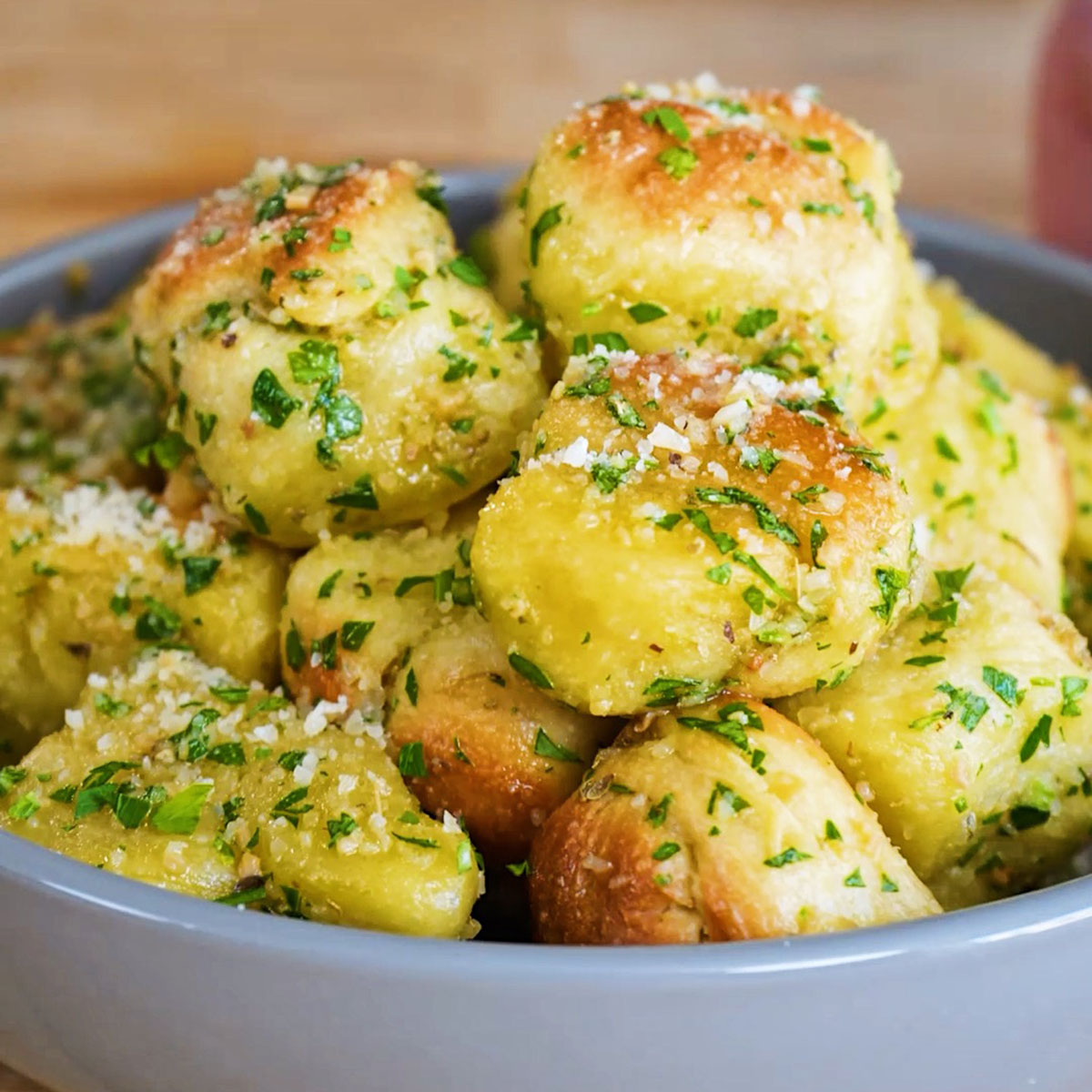 A grey bowl piled high with Dominos copycat garlic knots coated in a buttery parmesan and fresh herb sauce.