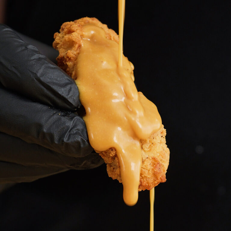 A close-up of a crispy fried chicken tender being generously coated with thick, creamy homemade Chick-fil-A sauce
