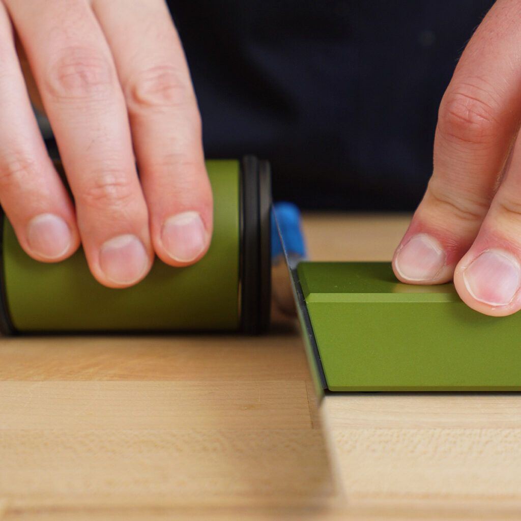 Cook using a green magnetic rolling knife sharpener on a chef's blade