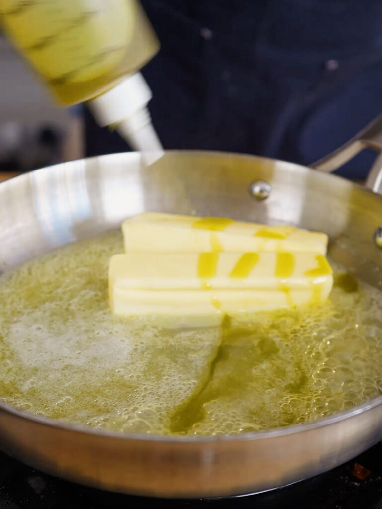 Adding olive oil to two sticks of melting butter in a hot pan to make the garlic knot sauce.
