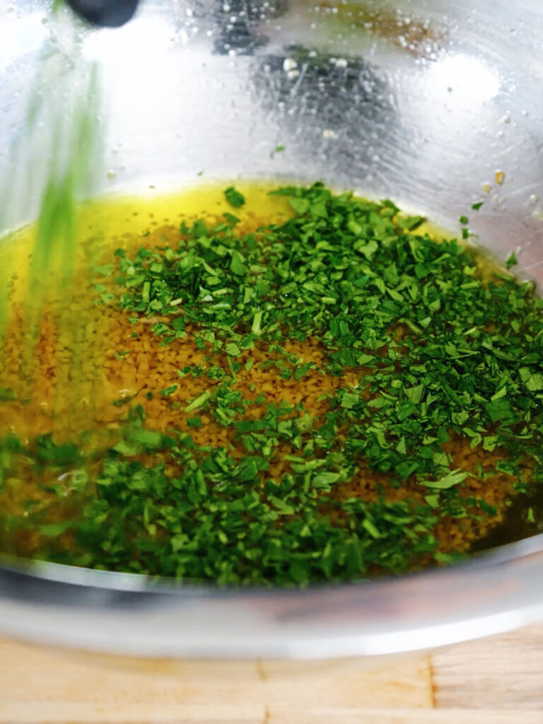 Whisking freshly chopped green parsley into a pan of melted garlic butter.