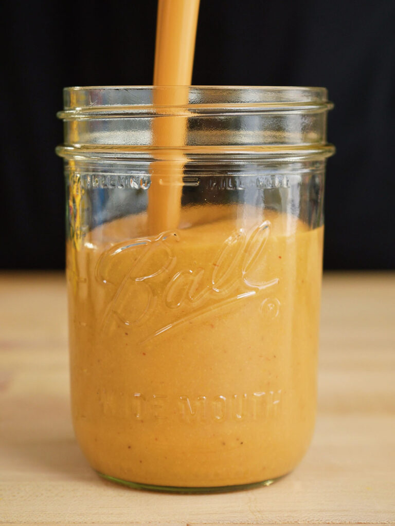 Pouring finished creamy copycat sauce into a glass Ball mason jar for storage