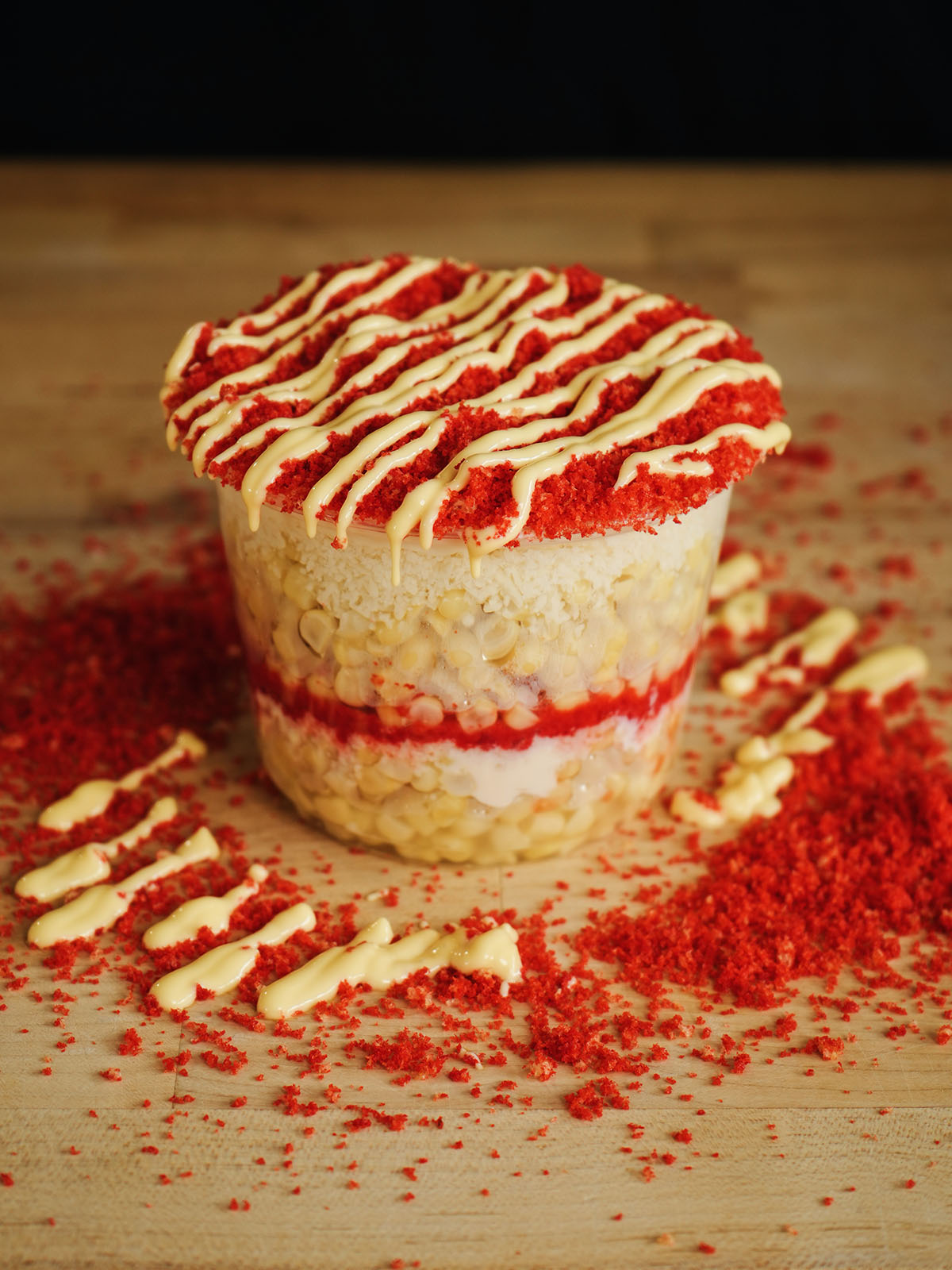An eye-level view of a homemade Mexican esquites recipe, highlighting the structural layers of sweet corn and savory toppings inside a clear 2-cup container.