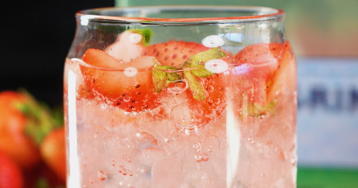 Close-up of the best homemade strawberry soda in a can-shaped glass, featuring fresh strawberry slices, ice cubes, and sparkling carbonation.
