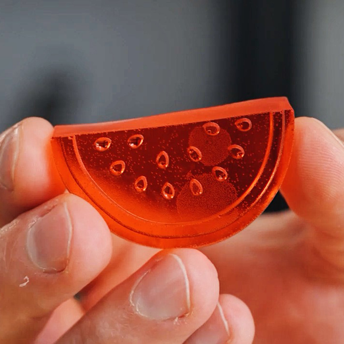Fingers holding a firm, uncoated watermelon slice gummy, ready to be tossed in a sour coating.