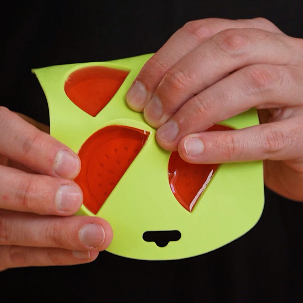 Hands carefully popping firm, red watermelon-shaped gummies out of a green silicone mold to make a Homemade Watermelon Sour Patch recipe.