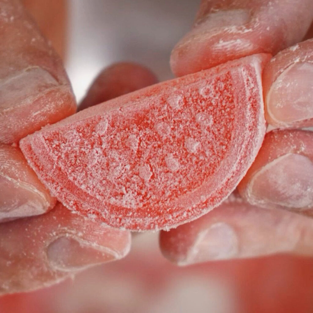 A close-up of a finished Homemade Watermelon Sour Patch candy, featuring a watermelon slice gummy perfectly coated in a dry, sour sugar mixture.